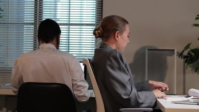 Businesswoman distracted by phone while male colleague works hard in the office, ignoring her work responsibilities