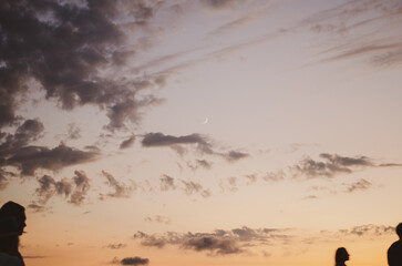Silhouettes of people watching a beautiful sunset from a viewpoint terrace with a crescent moon in the sky. © Nadia