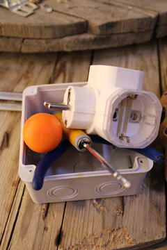 Electrical junction box with triple plug adapter and electrician tools on wooden table.