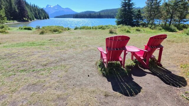 peaceful summer afternoon, with iconic red Adirondack chair overlooking the sparkling blue waters of Maligne Lake in Alberta of Canada in Jasper National Park