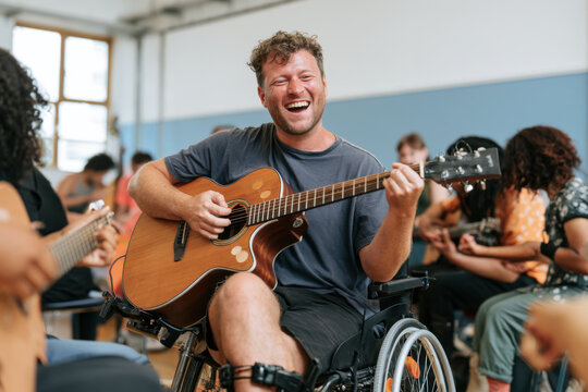 A joyful man in a wheelchair plays the acoustic guitar during an inclusive music workshop session