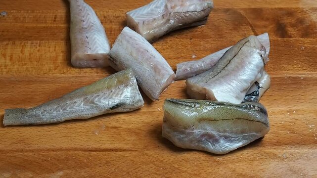 Pieces of sliced raw fresh Pollock fish on a wooden cutting board. Close up