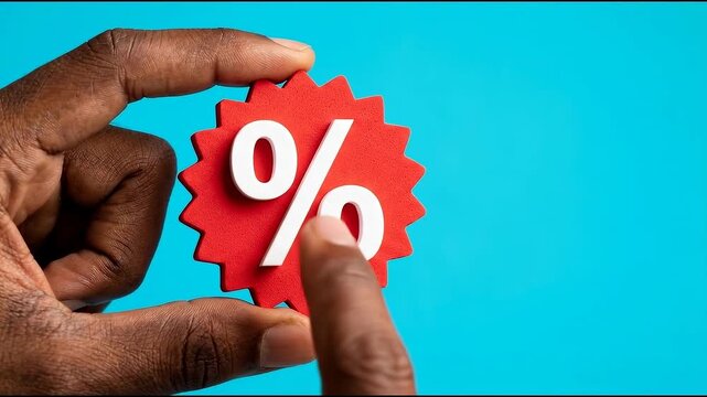 Dark-skinned hand holding a red percentage sign against a vibrant blue background, symbolizing discounts, sales, or interest rates