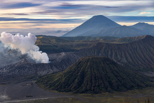 Mount Bromo volcano at sunrise, viewed from King Kong viewpoint in Bromo Tengger Semeru National Park, East Java, Indonesia. Active crater smoke, Mount Semeru cone, clouds, and vast ash plain.