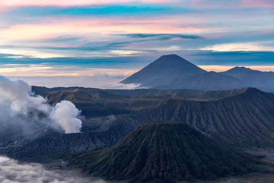 Mount Bromo volcano at sunrise, viewed from King Kong viewpoint in Bromo Tengger Semeru National Park, East Java, Indonesia. Active crater smoke, Mount Semeru cone, clouds, and vast ash plain.