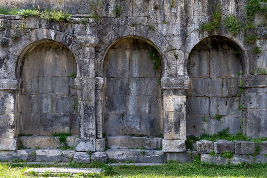 Close view of three rounded stone arches with weathered blocks and carved Armenian inscriptions and small plants growing along the ancient wall at Tatev Monastery, Tatev, Armenia