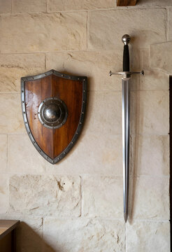 Medieval history and protection concept, antique wooden shield and steel longsword mounted on a rustic stone wall for heritage and fantasy decor