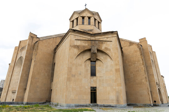 Rear apse and central dome with cross of Saint Gregory the Illuminator Cathedral rising above massive buttressed walls of pale tuff stone and a grassy foreground, Yerevan, Armenia