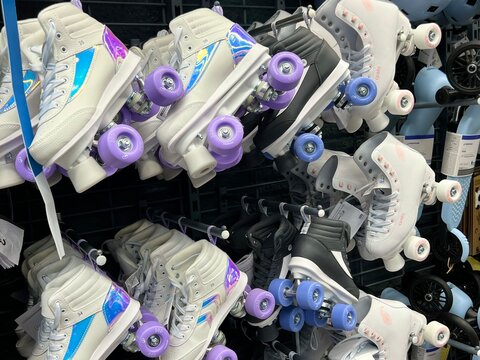 Many colorful quad roller skates hanging on display rack in sports equipment shop.
