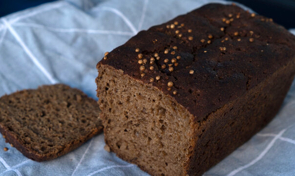 Traditional Borodinsky sourdough rye bread loaf with coriander seeds and a cut slice on a linen napkin.