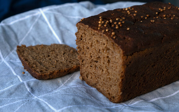 Traditional Borodinsky sourdough rye bread loaf with coriander seeds and a cut slice on a linen napkin.