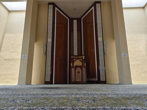 Low angle view from the prayer carpet of a mosque interior, showing the wooden pulpit and qibla direction