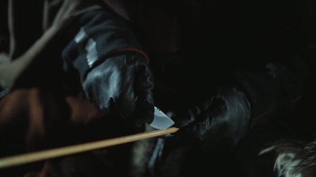 Person wearing black gloves sharpens small blade against wooden stick focusing closely on hand movements and tools in dim lighting knife sharpening tool