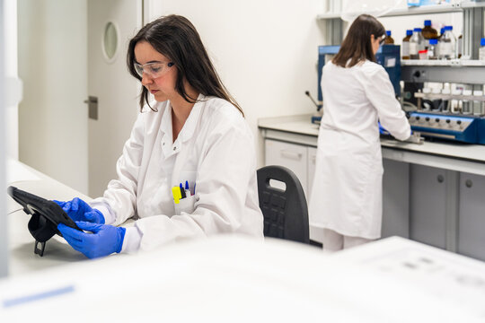 Scientist Works in Laboratory With Tablet and Colleague in Background