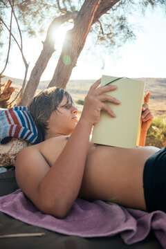 teenage boy absorbed in a book while relaxing beneath a tree