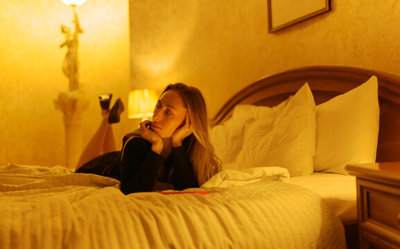 Woman Relaxes on a Bed in a Warmly Lit Room During the Evening