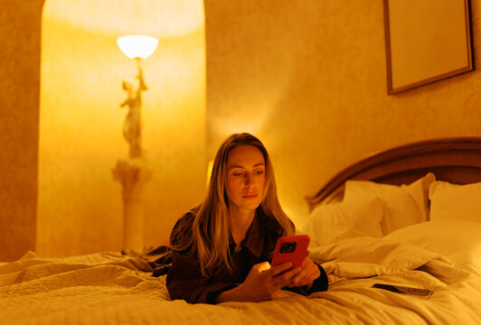 Woman Using Smartphone on Bed in Softly Lit Room