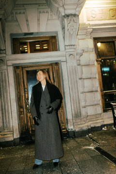 Woman Stands Outside a Building at Night Wearing a Long Coat