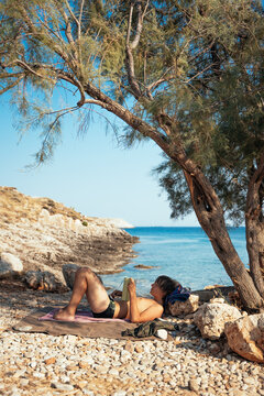 teenage boy resting beneath a coastal tree on a beach