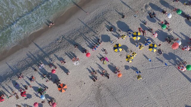 Top-down aerial view of colorful umbrellas and beachgoers on Copacabana Beach as waves roll onto the sand, Rio de Janeiro, Brazil.