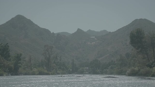 Misty mountains and green trees above a wide riverbed in morning light