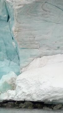 Vertical Video of Tall Narrow Iceberg Beside Floating Ice. White and blue ice, rippling water and soft diffuse light reveal natural frozen texture and sculpted contours across the marine scene.