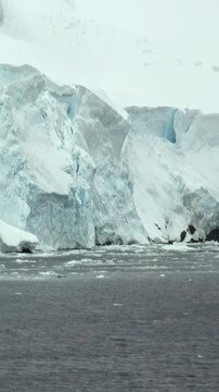 Vertical Video of Textured White Iceberg Above Dark Ocean Water. White and blue ice, rippling water and soft diffuse light reveal natural frozen texture and sculpted contours across the marine scene.