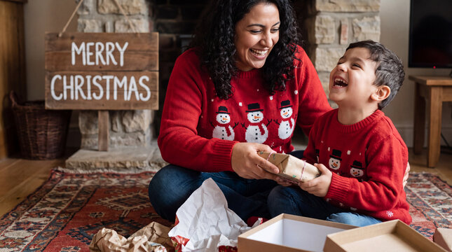 Soft morning light Christmas joy as a mother passes a present to her smiling son in snowman sweaters.