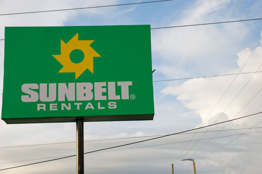 Sunbelt Rentals bright green sign and yellow sun logo mounted on a pole. Editorial Use Only October 4,  2026 Pinellas Park, FL USA set against a blue sky with clouds and intersecting power lines, conv