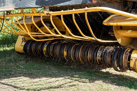 Detail of pickup mechanism and rotating tines of yellow agricultural hay baler in field