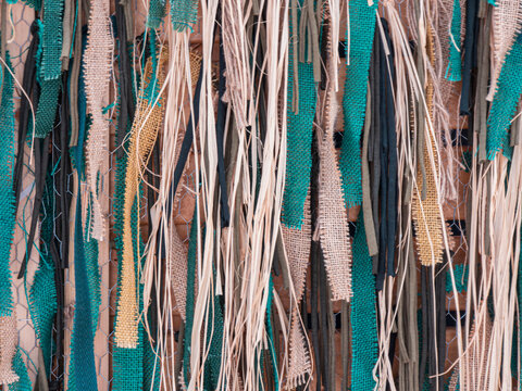 Decorative backdrop made of teal cloth strips, burlap fragments, and raffia strands on wire mesh