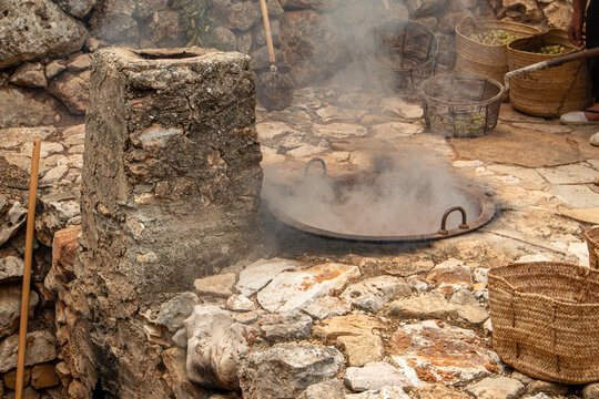 Traditional outdoor stone furnace with steam rising from a cauldron during the process of making raisins