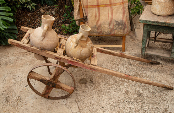 Antique wooden handcart with vintage clay water jugs on stone courtyard in a rustic setting