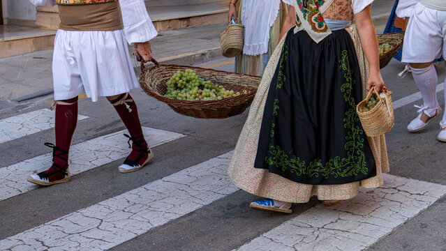 Participants in traditional costumes cross the street while carrying baskets filled with grapes in Spain