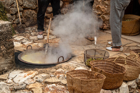 People operating a traditional stone cauldron during the escalda process with woven esparto baskets in a rural setting