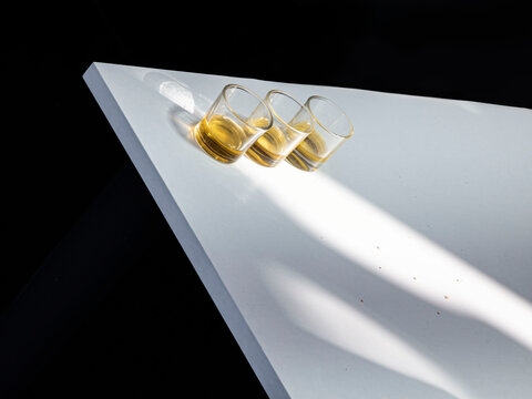 Small glass shots of olive oil on a white table in sunlight against a dark background