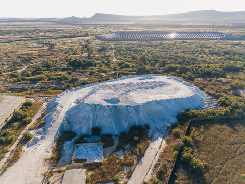 Aerial view of a large white industrial pile of limestone or chemical waste in an industrial landscape with surrounding vegetation and solar panels in Devnya, Varna, Bulgaria.