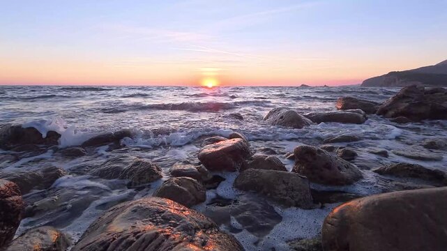 Sunset over rocky low tide shoreline with shimmering surf and warm orange sky reflecting on wet boulders timelapse
