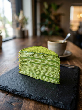 A delicious slice of matcha green tea crepe cake served on a slate plate in a cafe.