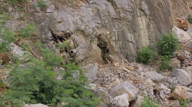 Special forces soldiers patrol through treacherous, rocky terrain during a clandestine mission, showcasing teamwork and military strategy in a hostile environment.