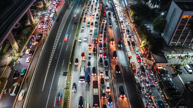 Aerial view of a busy highway at night featuring heavy traffic with glowing light trails from vehicles moving through the urban landscape of Jakarta, Indonesia.