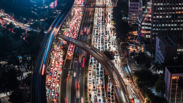 Aerial view of a busy highway interchange at night with light trails from heavy traffic and surrounding skyscrapers in Jakarta, Indonesia.