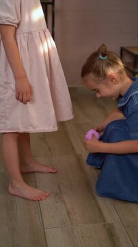 Two little sisters playing with a spiky massage ball for flatfoot prevention in a cozy living room