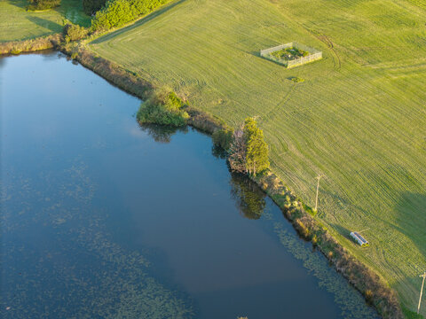 Aerial view of a calm pond bordered by lush green fields and trees in Melbourne, VIC, Australia.