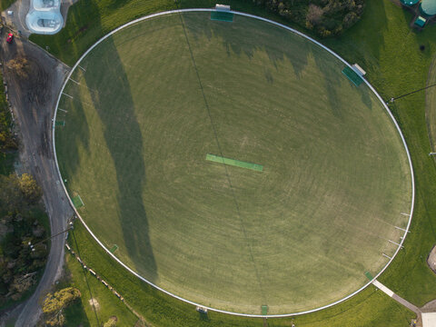 Aerial view of a cricket oval with a central pitch surrounded by green grass and trees in Melbourne, VIC, Australia.