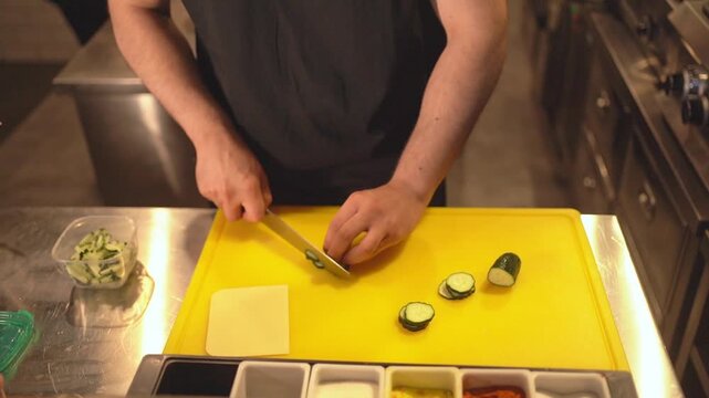 Chef slicing fresh zucchini on a yellow cutting board in a professional kitchen