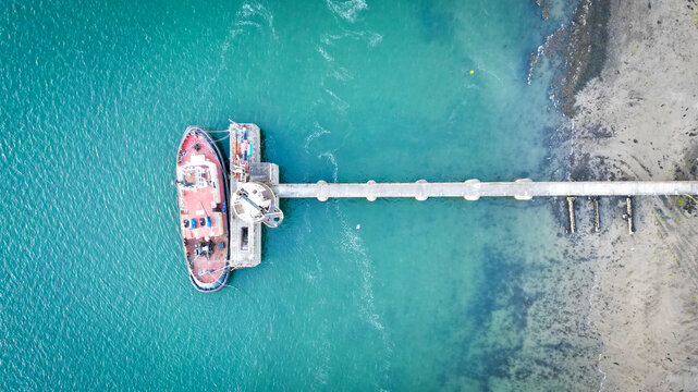 Aerial view of Instow Pier with a boat docked at the end of the pier extending into the turquoise water near the sandy beach in Instow, Devon, United Kingdom.