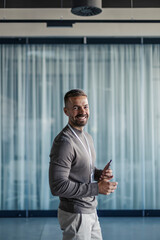 Fototapeta premium Smiling man standing in modern office holding phone