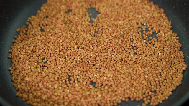 Roasting buckwheat grains in a frying pan, spreading by hand
