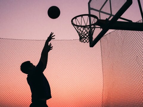Silhouette of basketball player shooting at sunset